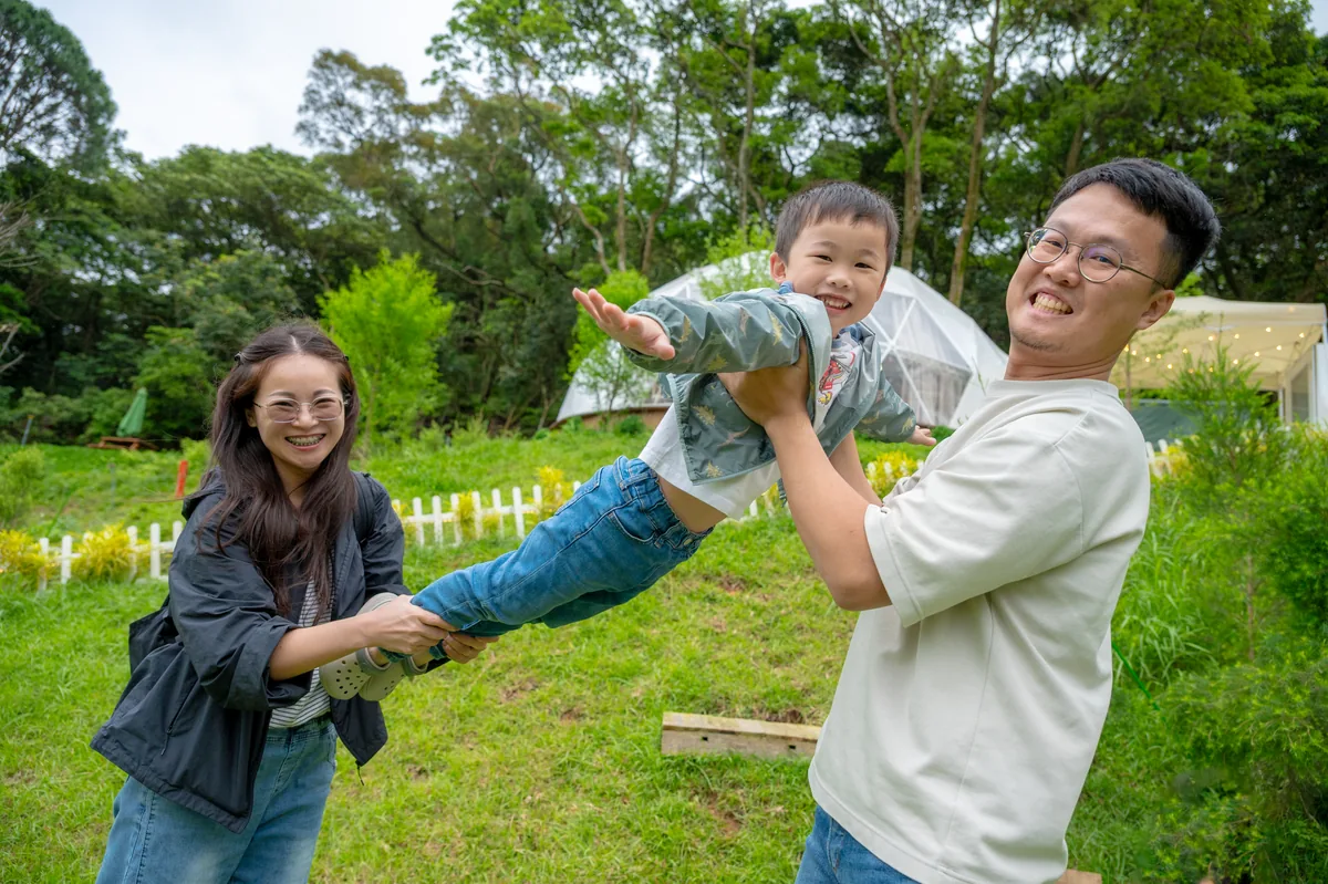 爸爸媽媽牽著兒子的手在草地玩飛高高